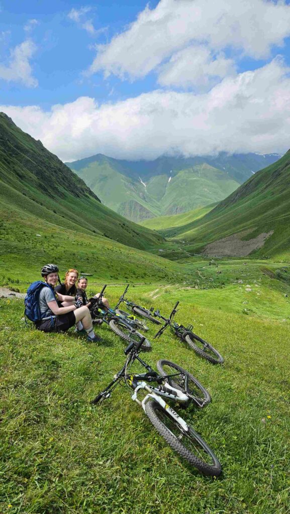 Mountain bikers at an alpine lake in Juta Valley with Caucasus peaks in the background