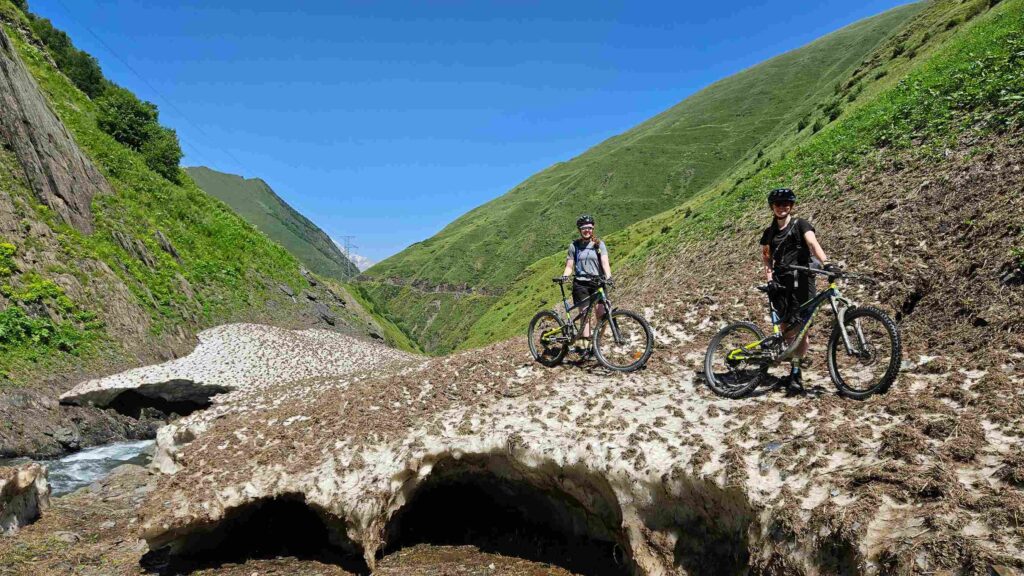 Riding past a massive summer snow bridge over a mountain stream.