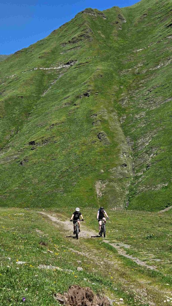 Mountain bikers on the Gudamakari trail with rocky Caucasus ridgeline above