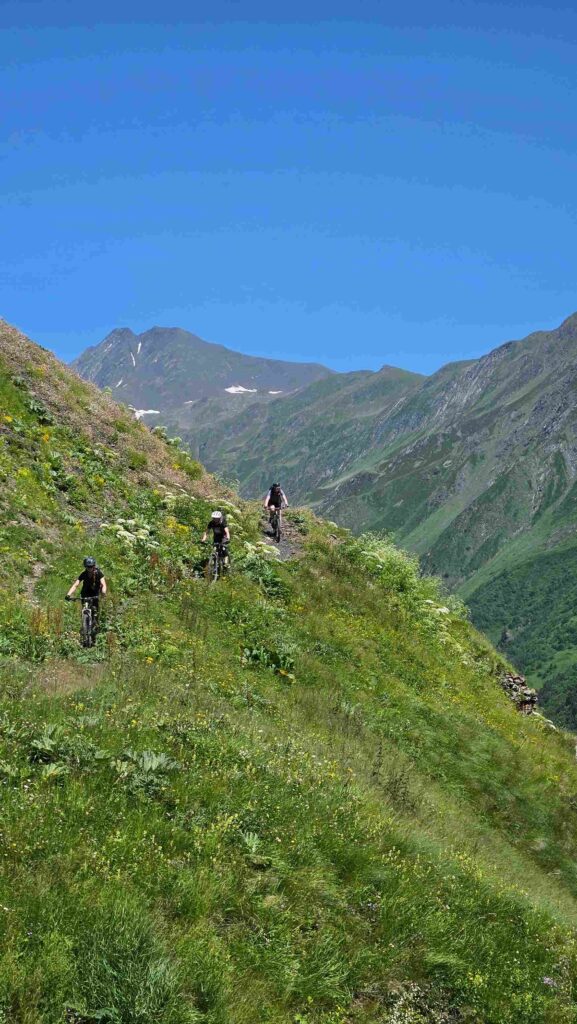 Group of MTB riders on a narrow trail with Caucasus peaks in the background, Georgia